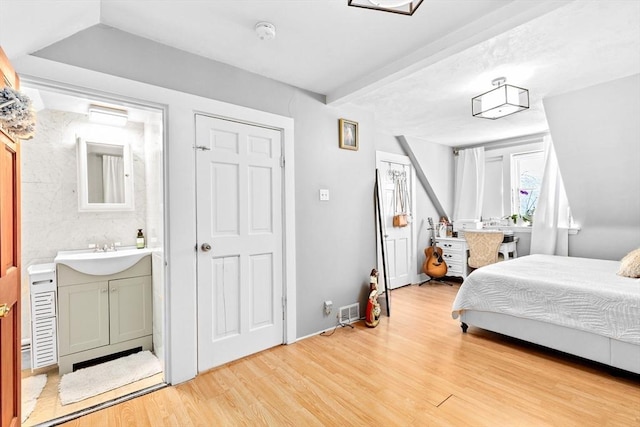 bedroom with light wood-style flooring, beamed ceiling, and a sink
