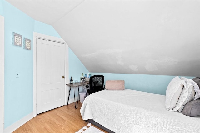 bedroom featuring baseboards, wood finished floors, and vaulted ceiling