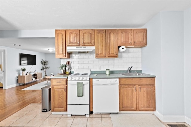 kitchen featuring a sink, under cabinet range hood, white appliances, tasteful backsplash, and baseboards
