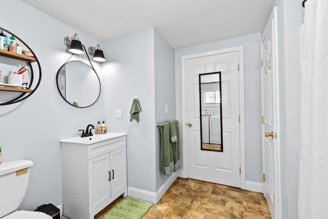 bathroom featuring toilet, stone finish flooring, vanity, and baseboards