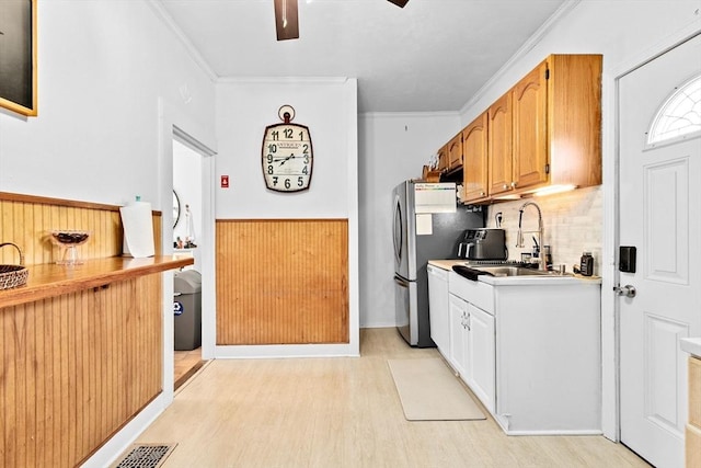 kitchen featuring crown molding, light wood-style flooring, ceiling fan, a wainscoted wall, and backsplash