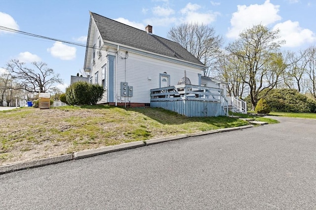 view of side of home featuring a deck, a chimney, a shingled roof, and a lawn