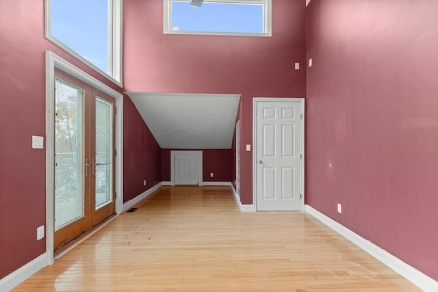 bonus room with light wood-type flooring, a high ceiling, and french doors