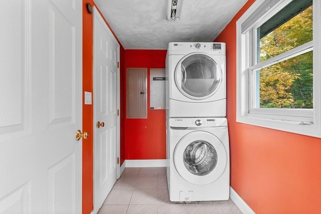 clothes washing area featuring electric panel, plenty of natural light, stacked washer and clothes dryer, and light tile patterned flooring