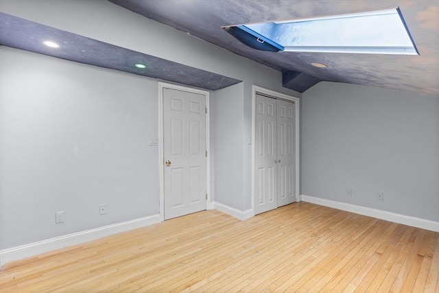 additional living space featuring lofted ceiling with skylight and light hardwood / wood-style flooring