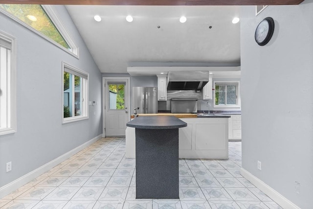 kitchen featuring sink, wall chimney exhaust hood, stainless steel fridge, vaulted ceiling, and white cabinets