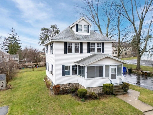 traditional style home with entry steps, a sunroom, a shingled roof, and a front yard