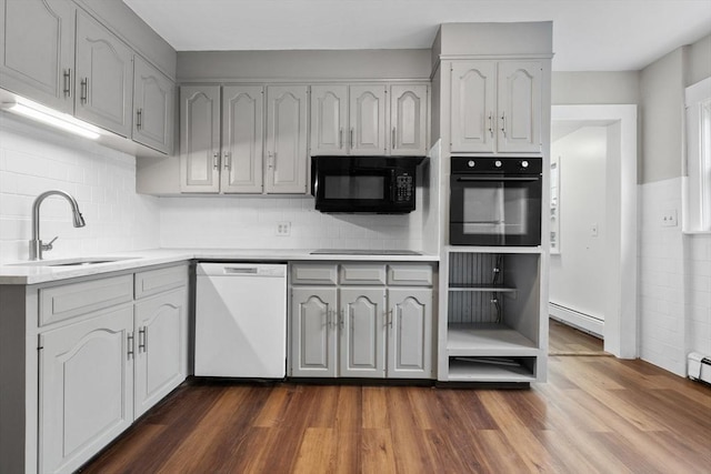 kitchen with light countertops, a sink, black appliances, gray cabinetry, and dark wood-style floors