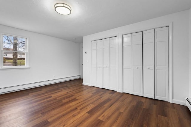 unfurnished bedroom with a baseboard heating unit, dark wood-type flooring, two closets, baseboard heating, and baseboards