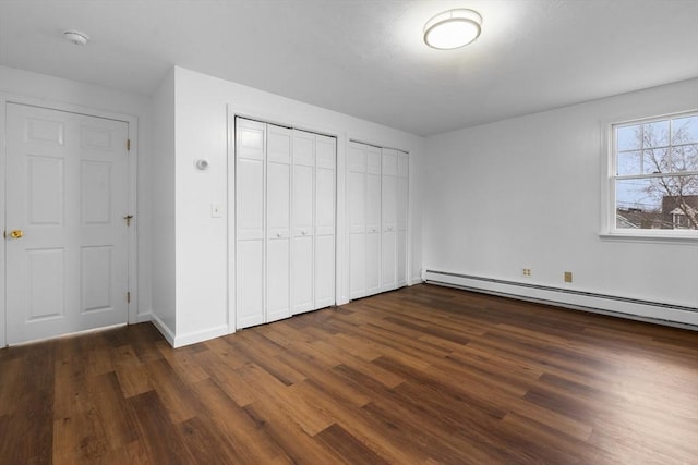 unfurnished bedroom featuring dark wood-style flooring, a baseboard radiator, and multiple closets