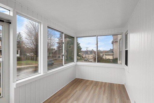 unfurnished sunroom featuring wood walls, plenty of natural light, and wood finished floors