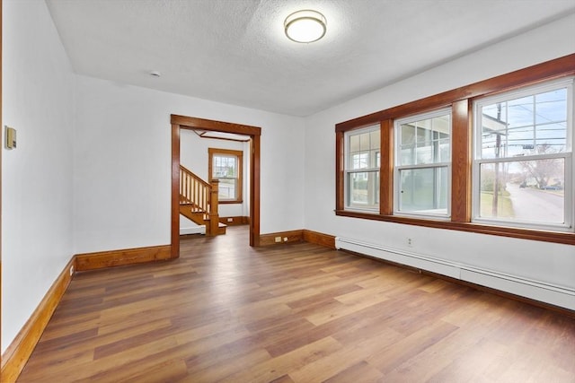 empty room featuring baseboards, a baseboard heating unit, a textured ceiling, and wood finished floors