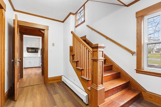 stairs with ornamental molding, wood finished floors, baseboards, and a baseboard heating unit