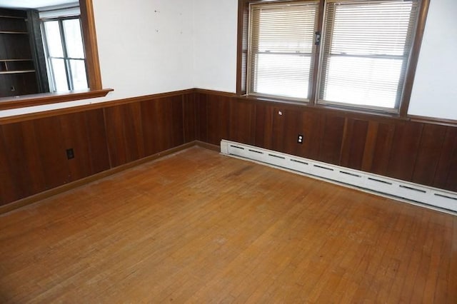 unfurnished room featuring a baseboard radiator, plenty of natural light, wainscoting, and hardwood / wood-style flooring