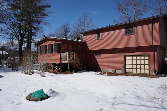 snow covered house with stairs, a garage, and a sunroom