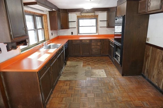 kitchen featuring wooden walls, a sink, light countertops, black appliances, and open shelves