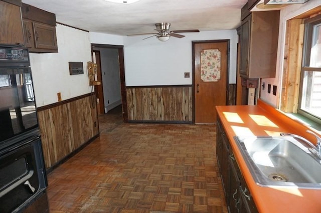 kitchen with ceiling fan, wooden walls, a wainscoted wall, and a sink