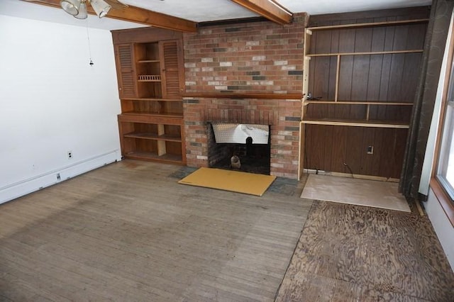 unfurnished living room with beam ceiling, a baseboard heating unit, wood finished floors, a fireplace, and baseboards