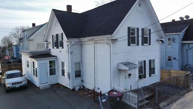 exterior space featuring a chimney, roof with shingles, and fence