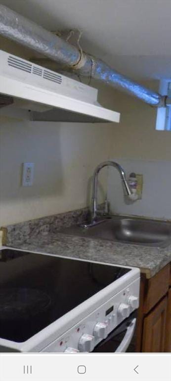 kitchen with under cabinet range hood, white electric range, brown cabinetry, and a sink