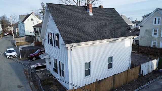 view of property exterior with a chimney, roof with shingles, and fence