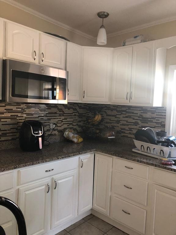 kitchen with stainless steel microwave, backsplash, ornamental molding, and light tile patterned flooring