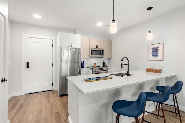 kitchen featuring a peninsula, a kitchen breakfast bar, a sink, light wood-style flooring, and stainless steel appliances