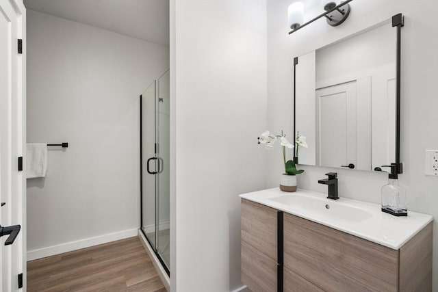 bathroom featuring baseboards, a shower stall, wood finished floors, and vanity
