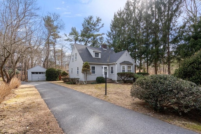 cape cod-style house with roof with shingles, a chimney, a garage, an outdoor structure, and driveway