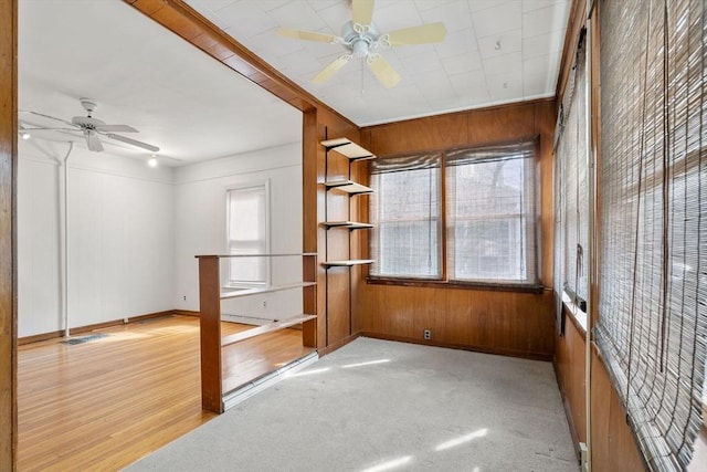 unfurnished room with light carpet, visible vents, wood walls, and ceiling fan