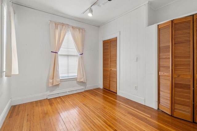 unfurnished bedroom with track lighting, baseboards, light wood-style floors, and a baseboard radiator