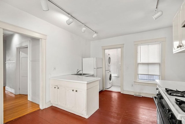 kitchen featuring a sink, light countertops, dark wood-style flooring, and stacked washing maching and dryer