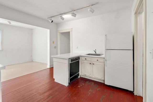 kitchen with a sink, black dishwasher, freestanding refrigerator, a peninsula, and light countertops