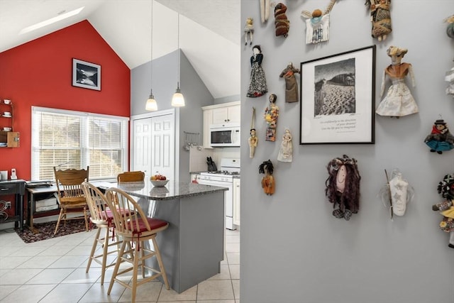 kitchen featuring a breakfast bar, decorative light fixtures, white cabinets, light tile patterned floors, and white appliances