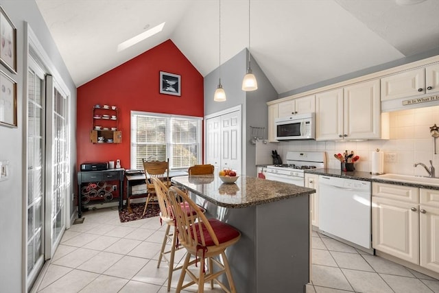 kitchen featuring sink, a breakfast bar area, a center island, white appliances, and cream cabinetry