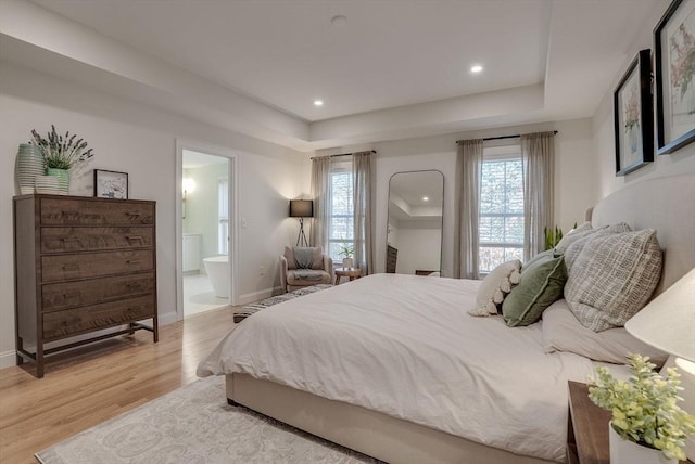 bedroom with ensuite bathroom, recessed lighting, baseboards, light wood-type flooring, and a tray ceiling