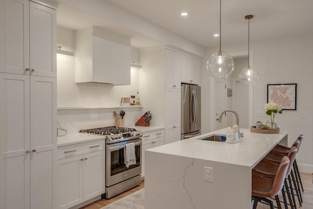 kitchen with light stone counters, stainless steel appliances, a sink, white cabinetry, and a center island with sink