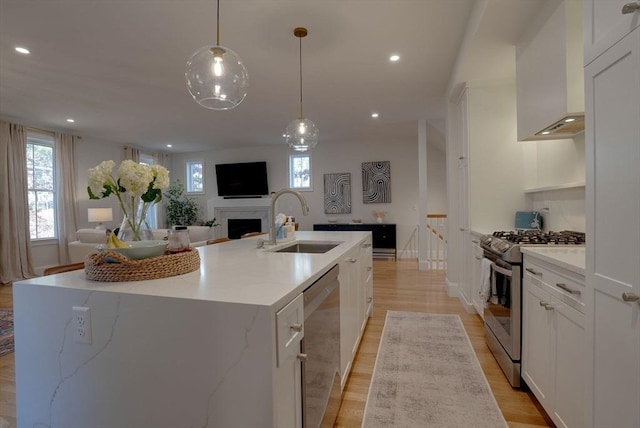 kitchen featuring stainless steel appliances, decorative light fixtures, a center island with sink, and a sink