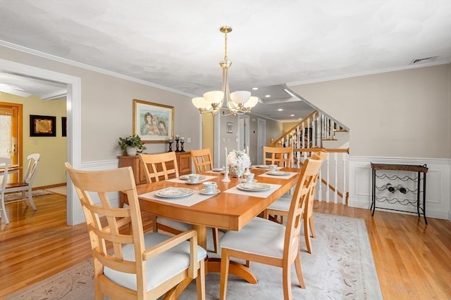 dining room with visible vents, light wood-style floors, ornamental molding, stairway, and an inviting chandelier