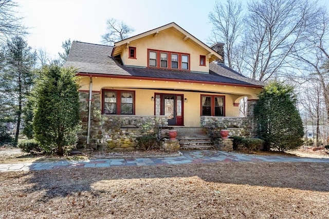 view of front of house with stone siding, stucco siding, a porch, and a chimney