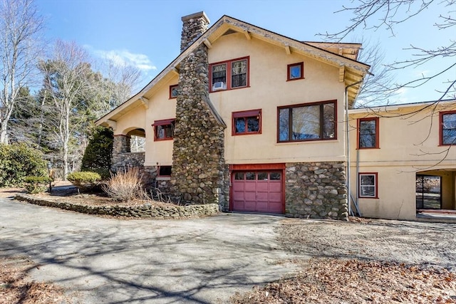 view of side of property with stucco siding, driveway, an attached garage, and a chimney