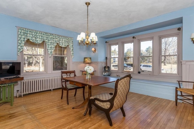 dining room featuring an inviting chandelier, hardwood / wood-style flooring, radiator heating unit, and wainscoting