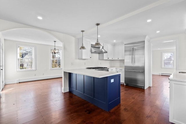 kitchen with a peninsula, arched walkways, stainless steel built in fridge, a baseboard heating unit, and wall chimney exhaust hood