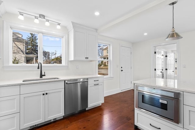 kitchen featuring dark wood finished floors, a sink, white cabinets, stainless steel dishwasher, and decorative light fixtures