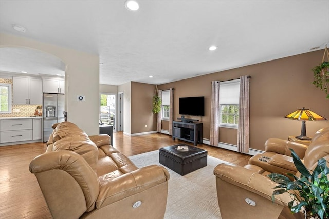 living room featuring light wood-type flooring, recessed lighting, arched walkways, and baseboards