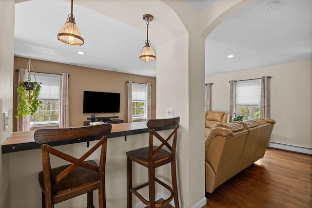 living room featuring wood finished floors, a baseboard heating unit, arched walkways, baseboards, and recessed lighting