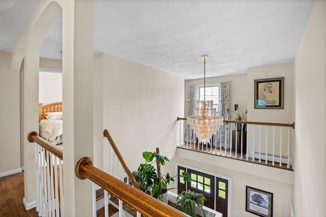 hall featuring a baseboard heating unit, a chandelier, an upstairs landing, arched walkways, and wood finished floors