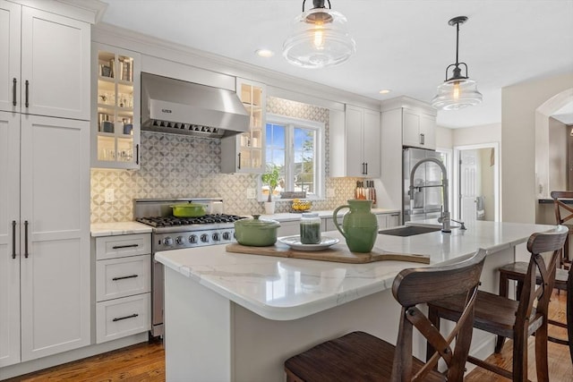 kitchen with extractor fan, stainless steel gas range, a breakfast bar, backsplash, and decorative light fixtures