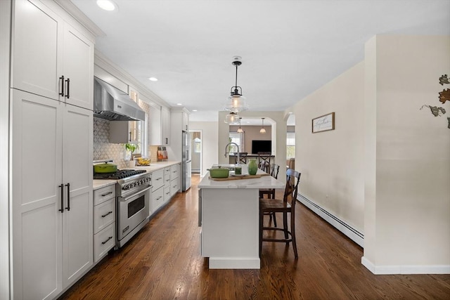 kitchen with appliances with stainless steel finishes, wall chimney range hood, a baseboard heating unit, a kitchen bar, and backsplash