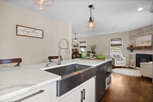 kitchen featuring a sink, light stone counters, dishwasher, dark wood-style flooring, and pendant lighting